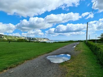 Road amidst grassy field against sky