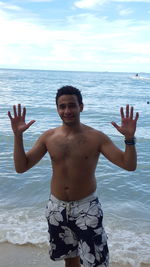 Portrait of young man standing at beach against sky