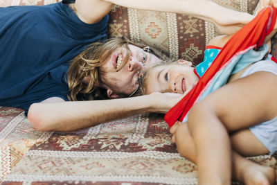 Happy father playing with daughter while lying on bed at home