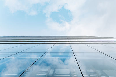 Low angle view of glass building against cloudy sky