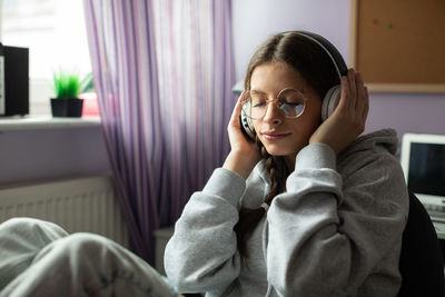 A teenage girl listens to music on wireless headphones with her eyes closed.