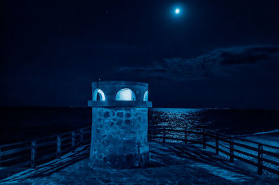 Built structure by sea against sky at night