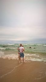 Rear view of friends standing on beach against sky