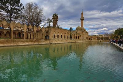 Mosque by lake against cloudy sky