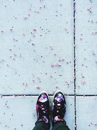 Low section of person surrounded by small cherry blossoms on footpath