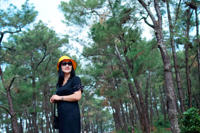 Portrait of woman standing by trees in forest