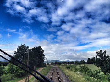 Railroad tracks on field against cloudy sky