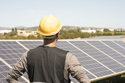 Rear view of male maintenance engineer looking at solar panels in field