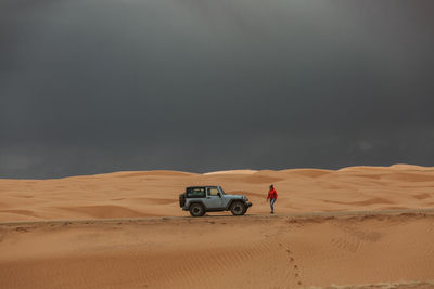 Woman walks back to jeep under stormy skies in utah sand dunes