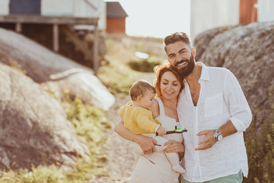 Portrait of smiling father standing by woman carrying baby girl over archipelago