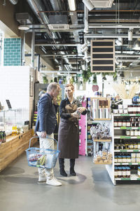 Female owner explaining product to mature man in organic supermarket