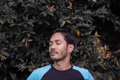 Young man with eyes closed against trees