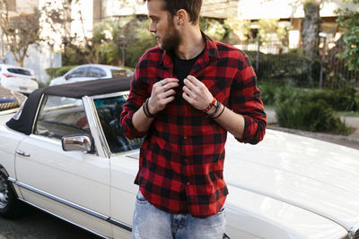 Man wearing plaid shirt while standing against car