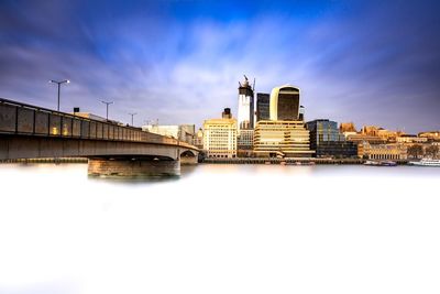 Bridge over river by buildings against sky