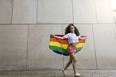 Woman holding rainbow flag while walking in front of wall