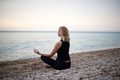 Full length of man sitting by sea against sky