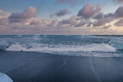 Scenic view of waves on black sand shore of diamond beach against sky at sunset