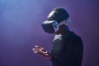 Astonished female african american gamer in modern vr goggles standing on dark background in studio while experiencing virtual reality in neon illumination