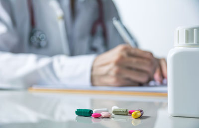 Close-up of doctor writing with medicine in foreground on table