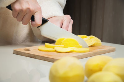 Young caucasian woman in a bathrobe stands and cuts potatoes on a cutting board