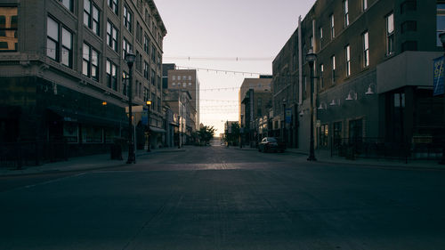 Empty road amidst buildings in city against clear sky