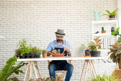 Portrait of young man using laptop while sitting against brick wall