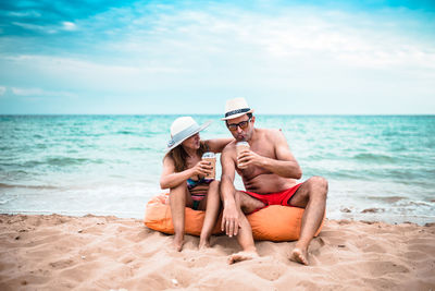 Mature couple having drinks while sitting at beach