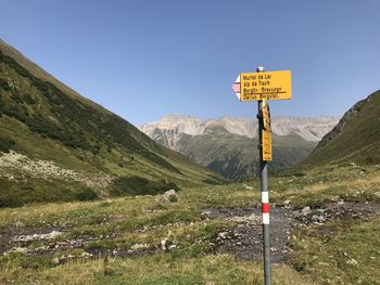 Road sign by mountains against clear sky