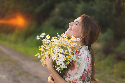 Portrait young beautiful woman with chamomile flowers at sunset.