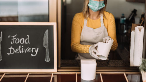 Midsection of woman wearing mask delivering food through window