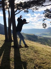 Man standing on tree by mountain against sky