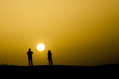 Silhouette people standing on landscape against orange sky