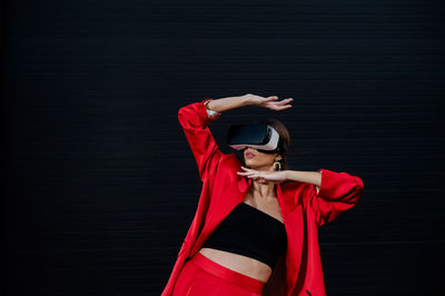 Elegant woman in a red suit using virtual reality goggles on a black background