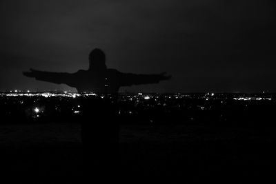 Rear view of silhouette man on illuminated beach against sky at night