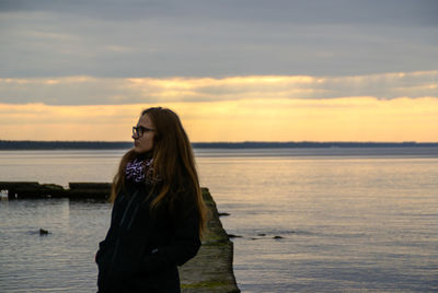 Young woman standing by sea against sky during sunset