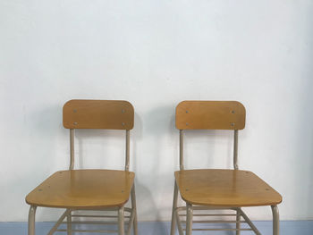 Two brown empty school chairs with a white wall on background in natural daylight, nostalgia concept