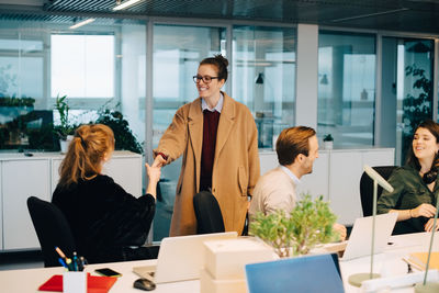 Smiling businesswoman greeting female professional sitting by colleagues at creative office