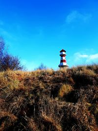 Lighthouse on landscape against blue sky