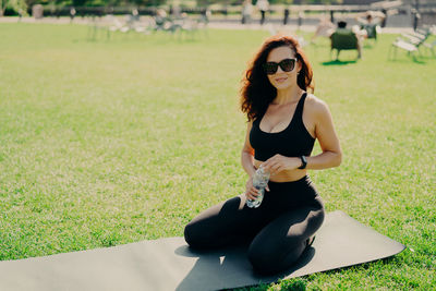 Portrait of woman wearing sunglasses kneeling on mat in park