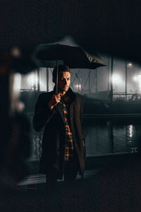 Man standing with umbrella by sea at night