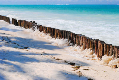 Wooden posts on beach by sea against sky