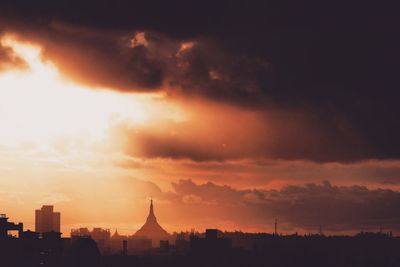 Silhouette of city against cloudy sky during sunset