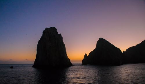 Silhouette rock in sea against sky during sunset