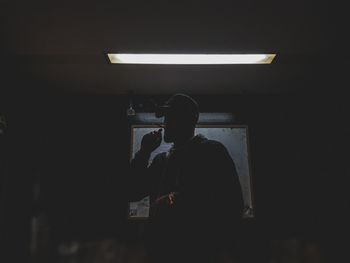 Rear view of silhouette man standing against wall in darkroom
