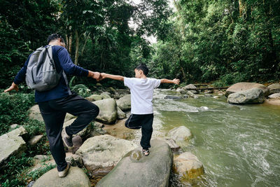 Rear view of friends standing on rock by stream