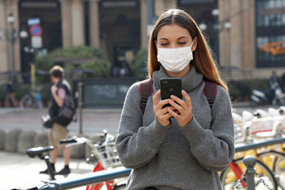 Young woman wearing mask using smart phone while standing on road