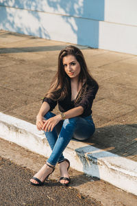 Portrait of young woman sitting on footpath in city