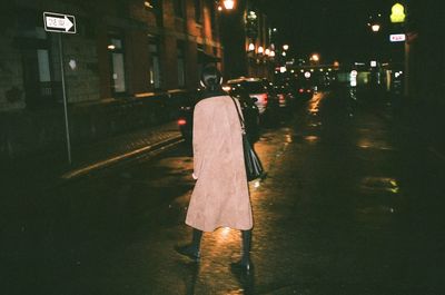 Rear view of woman walking on illuminated street at night