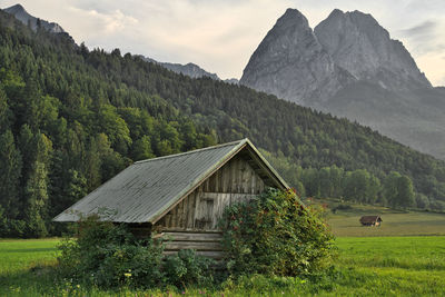 House on field by mountain against sky