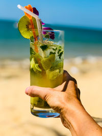 Cropped image of hand holding drink at beach
